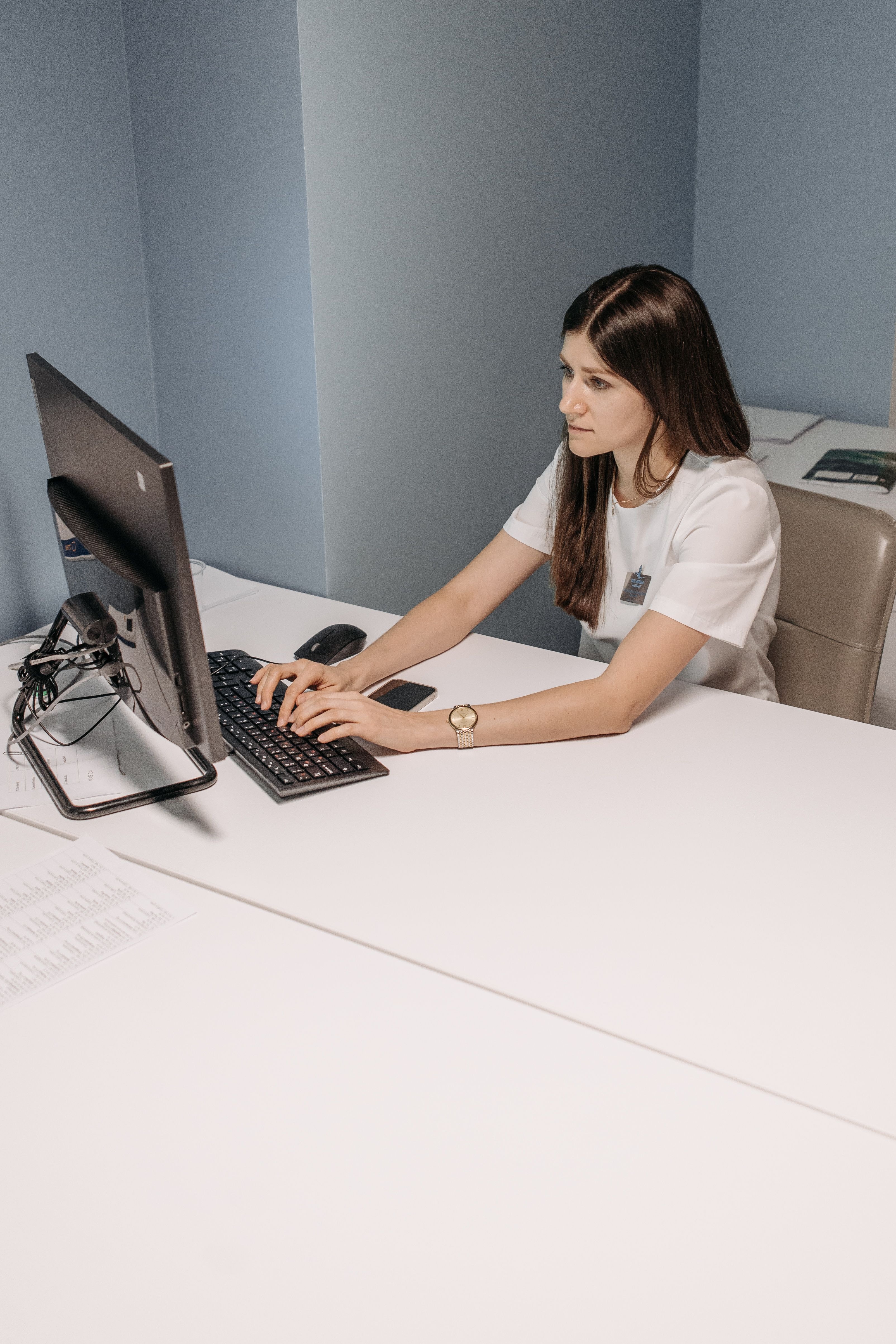 Klinikmedarbejder arbejder ved computer i et konsultationsrum.
