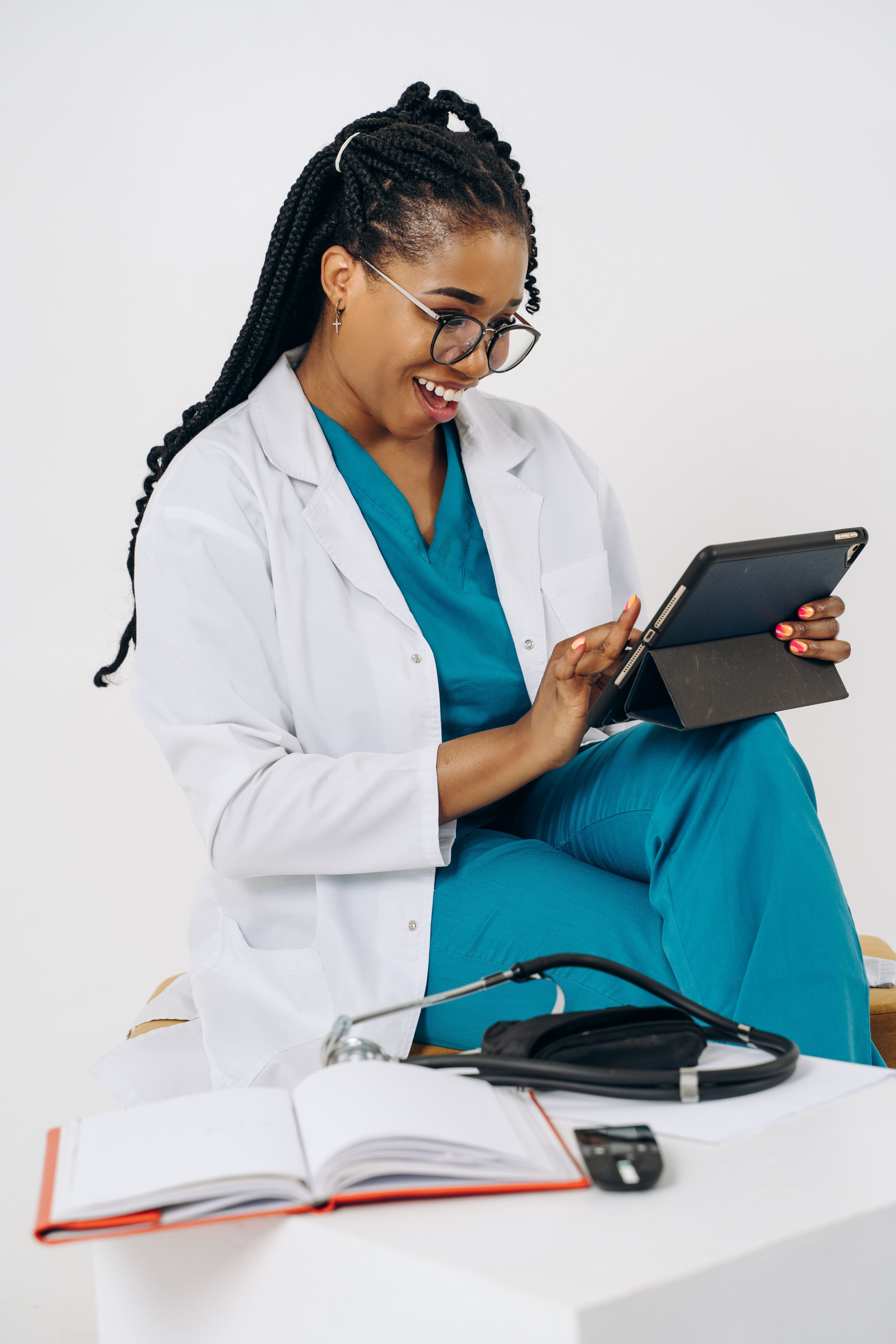Sundhedsperson i kliniktøj bruger en tablet ved et bord.