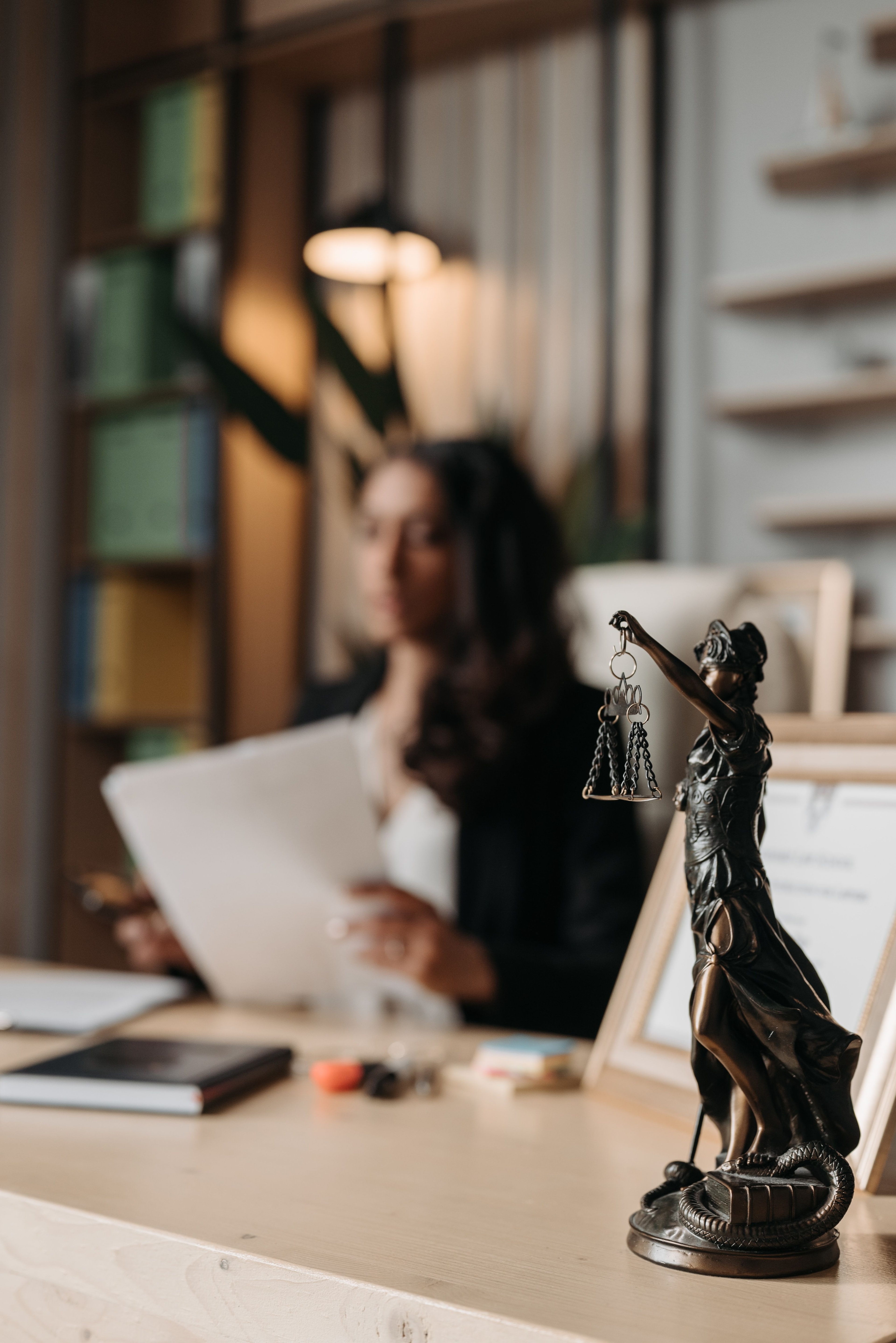 Retfærdighedsfigur i forgrunden og en person ved et skrivebord.