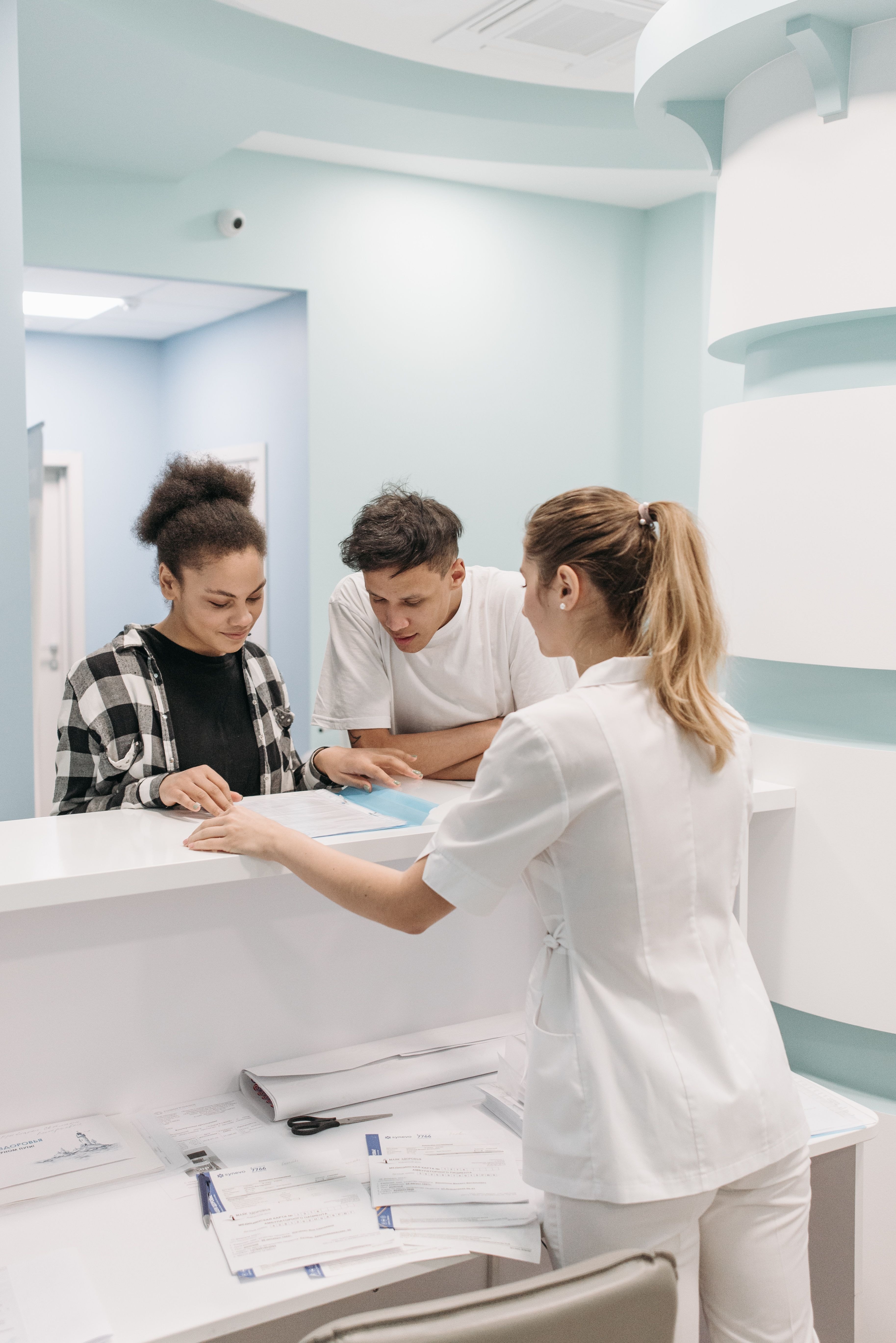 Klinikmedarbejder taler med to personer ved receptionen.