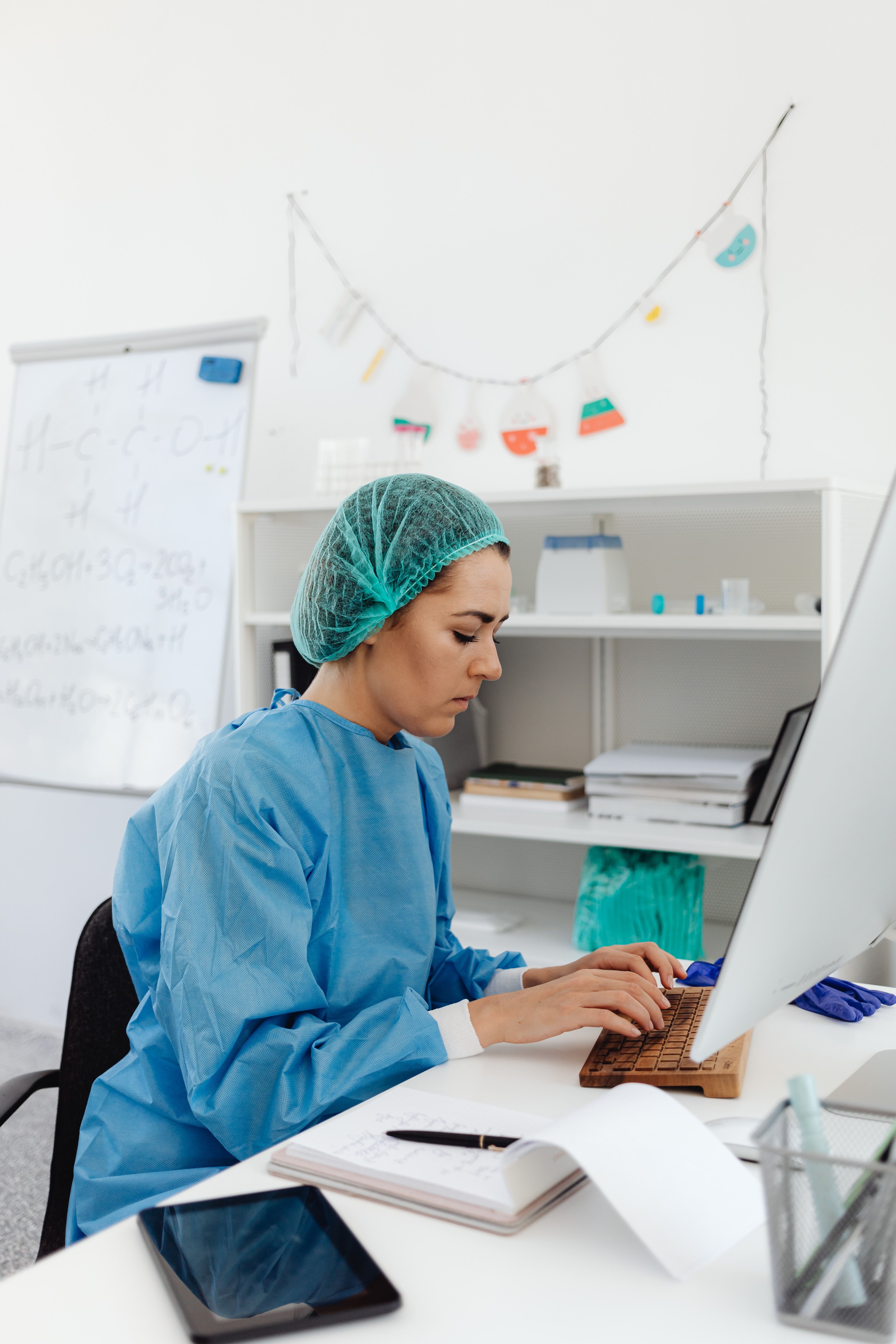 Klinikmedarbejder i blåt arbejdstøj skriver ved en computer.